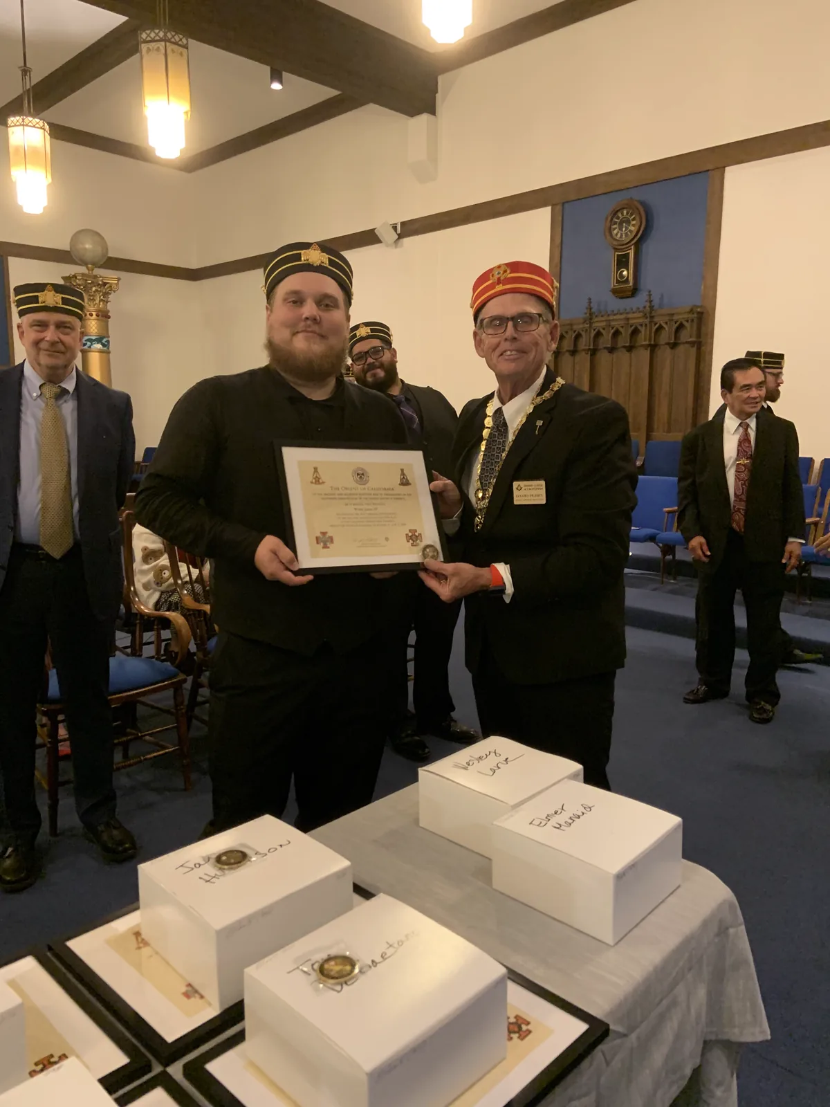 An officer presenting an Order of California certificate and coin to a new member, with engraved cap boxes on the table