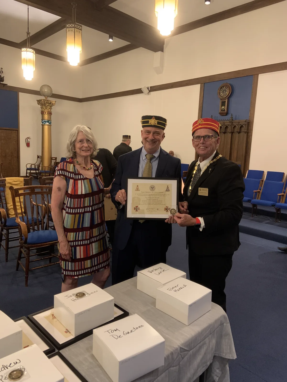 An officer presenting a certificate and coin to a new member, with his wife beside him